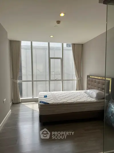 Spacious bedroom with large window and modern decor in a high-rise apartment.