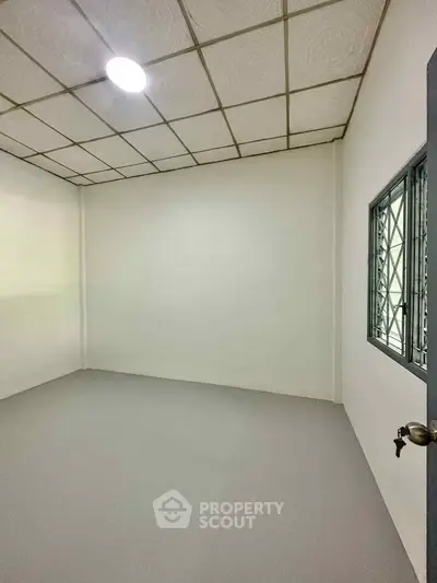 Minimalist empty room with white walls and ceiling, featuring a single window and light fixture.