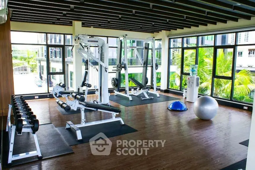 Spacious gym with modern equipment and large windows offering lush green views.