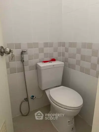 Compact bathroom with modern toilet and bidet spray in a tiled setting.