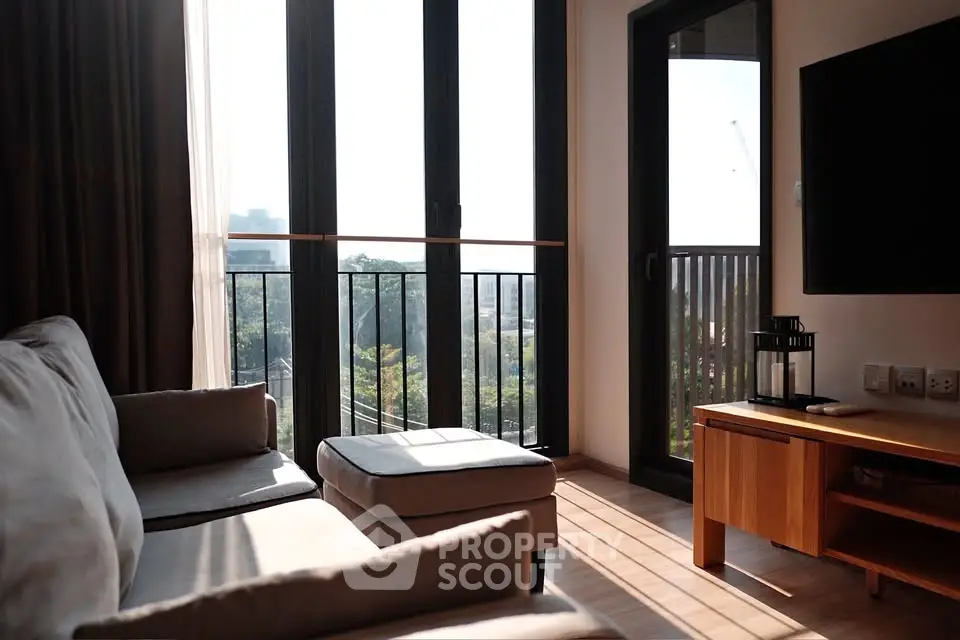 Bright living room with large windows and balcony view, featuring modern furniture and natural light.