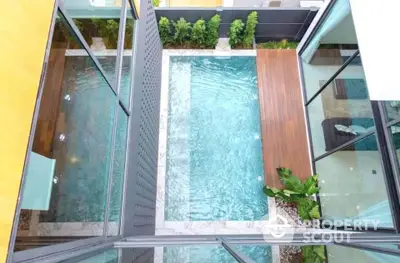 Stunning aerial view of modern private pool with wooden deck and lush greenery, perfect for relaxation.