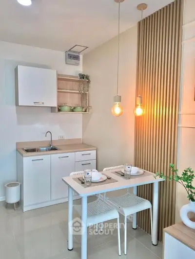 Modern kitchen with sleek white cabinets and cozy dining area, featuring stylish pendant lighting and wooden accents.