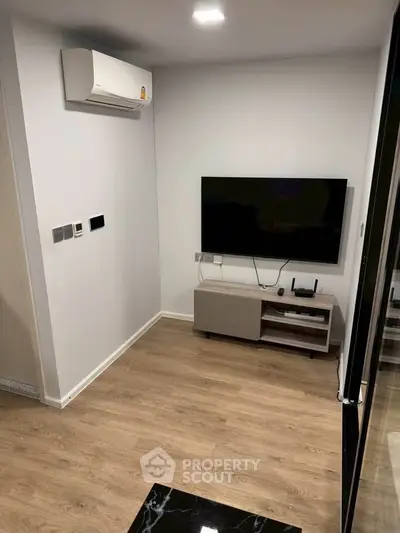 Modern living room with wall-mounted TV and air conditioning, featuring sleek wooden flooring.