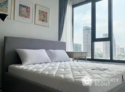 Spacious bedroom with a large window offering a stunning cityscape view, complemented by modern art and a plush bed, ideal for urban living.