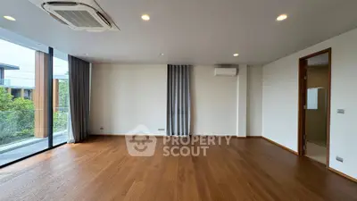 Spacious empty living room with wooden flooring and large windows overlooking greenery.