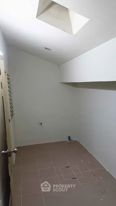 Compact storage room with tiled floor and skylight, ideal for organizing household items.