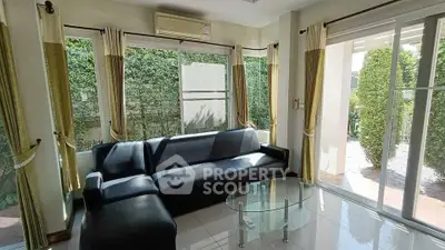 Spacious living room with large windows and garden view, featuring modern black sofa and glass coffee table.
