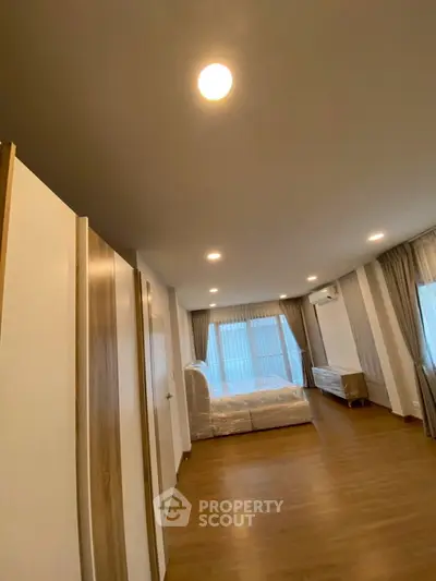 Spacious bedroom with wooden flooring and large windows for natural light.