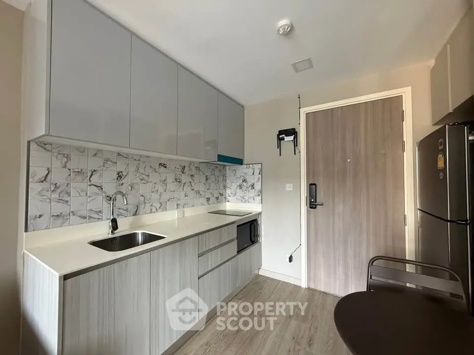 Modern kitchen with sleek cabinetry and marble backsplash in a compact apartment setting.