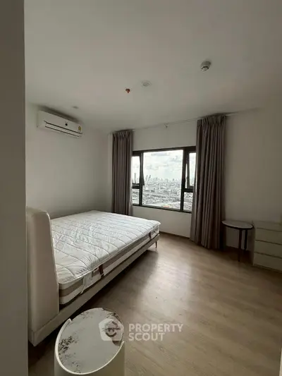 Spacious bedroom with city view, featuring modern furnishings and large window for natural light.