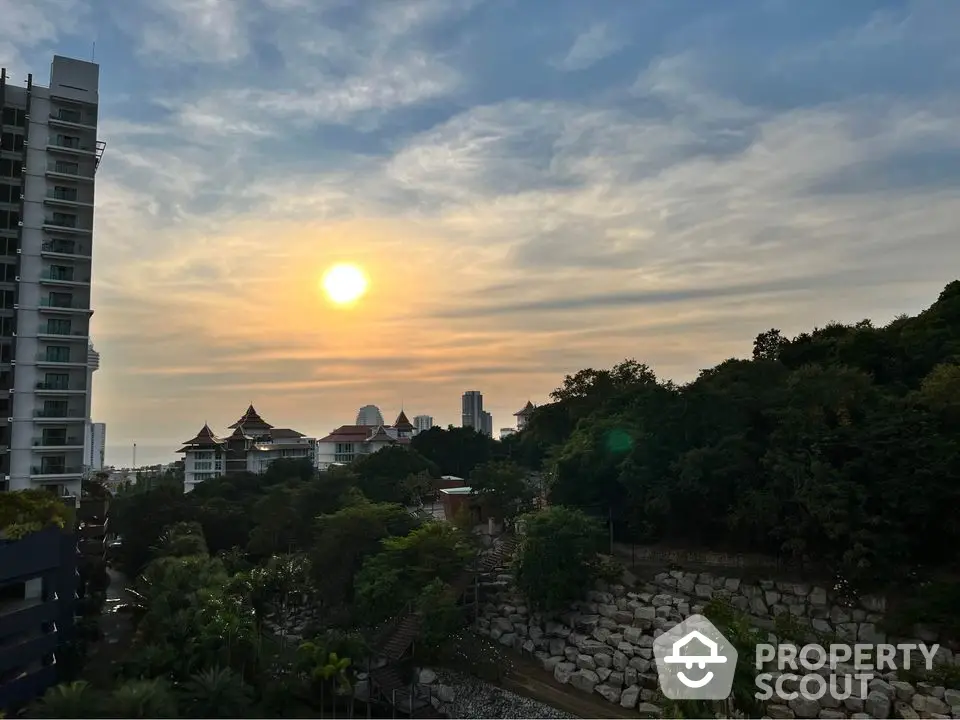 Stunning sunset view from a high-rise building overlooking lush greenery and city skyline.