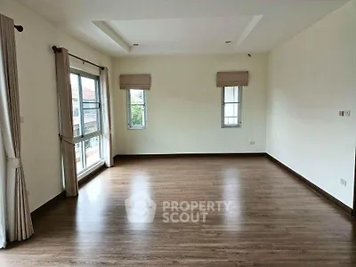 Spacious empty room with wooden flooring and large windows for natural light.