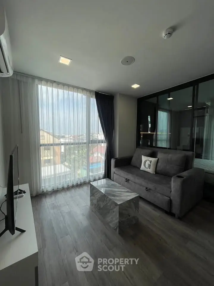 Modern living room with sleek gray sofa, marble coffee table, and large window with city view.