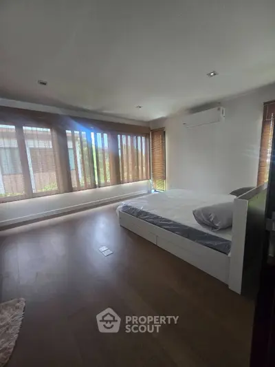 Spacious bedroom with large windows and modern decor, featuring hardwood floors and natural light.