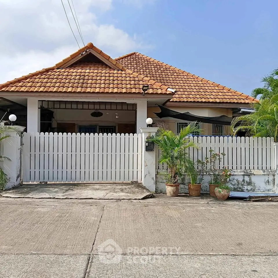 Charming single-story house with red-tiled roof and white picket fence, perfect for family living.