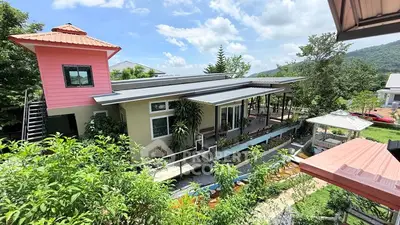 Charming modern house with lush garden and mountain views, featuring a unique architectural design and outdoor seating area.