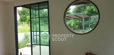 Modern room with circular window and sliding glass door opening to lush garden view.