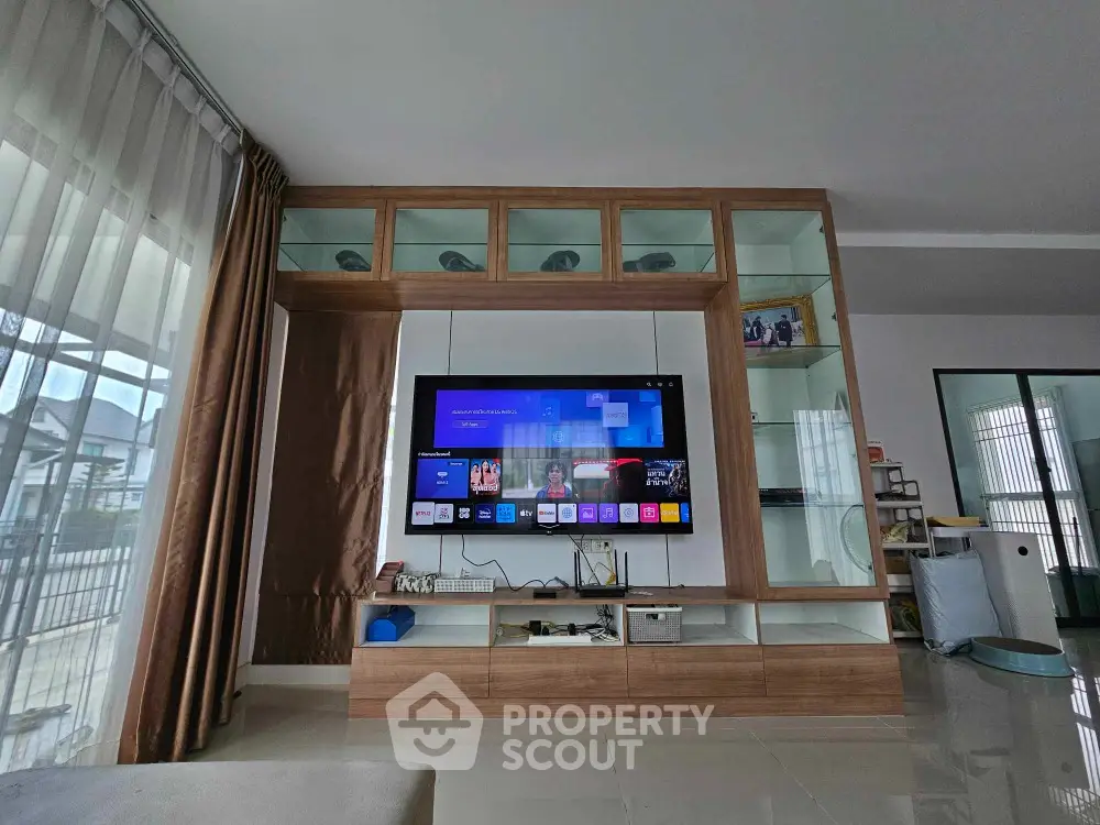 Spacious living room with modern entertainment unit, ample shelving, and large windows allowing for natural light.