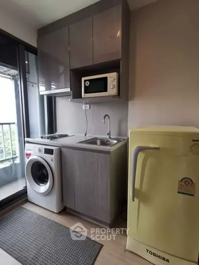 Compact kitchen with washing machine, microwave, and fridge in modern apartment.