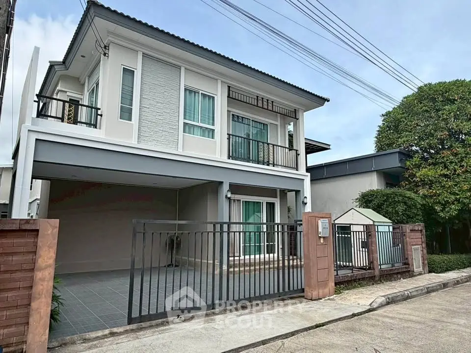 Modern two-story house with balcony and gated driveway in suburban neighborhood.
