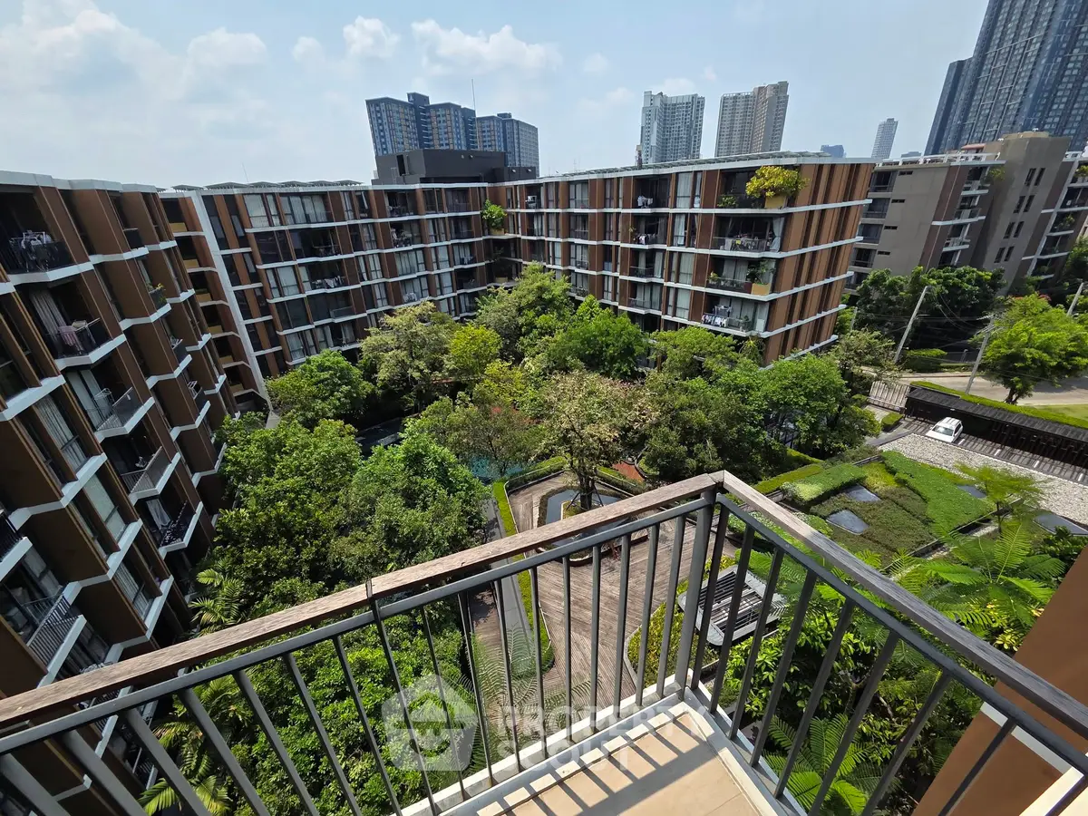 Stunning view from balcony overlooking lush garden and modern apartment complex.