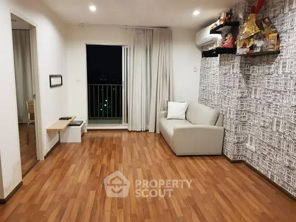 Spacious living room with wooden flooring and modern decor, featuring a cozy sofa and balcony access.
