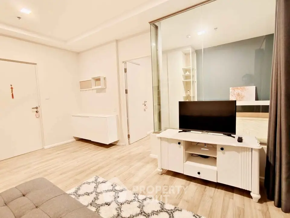 Modern living room with stylish decor and glass partition, featuring a cozy TV setup and elegant flooring.