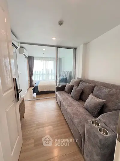Modern apartment with cozy living room and bedroom, featuring stylish gray sofa and wooden flooring.