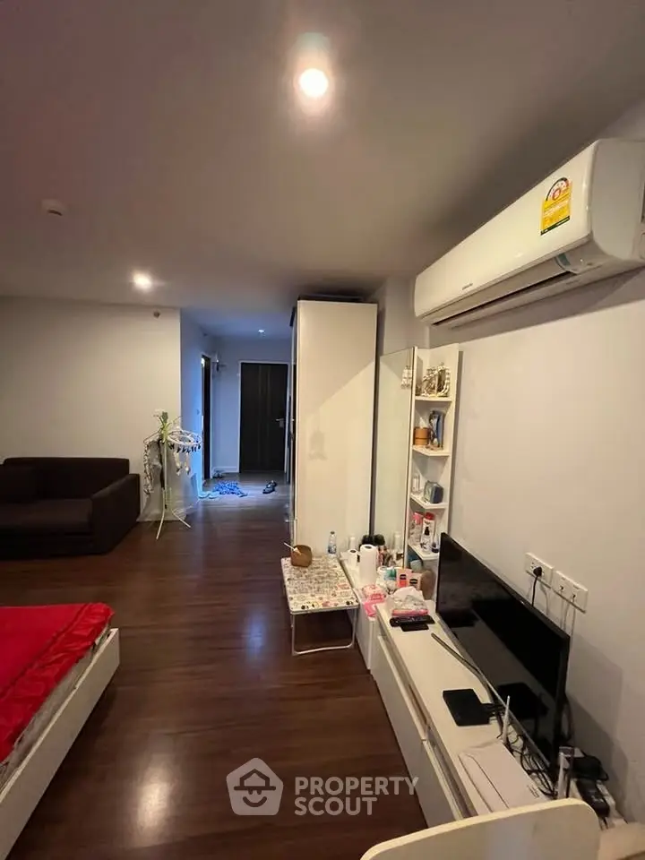 Modern studio apartment with sleek wooden flooring and cozy furnishings, featuring a wall-mounted air conditioner and TV unit.