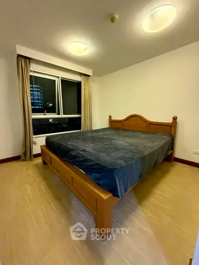 Spacious bedroom with large window and elegant wooden bed frame in modern apartment.