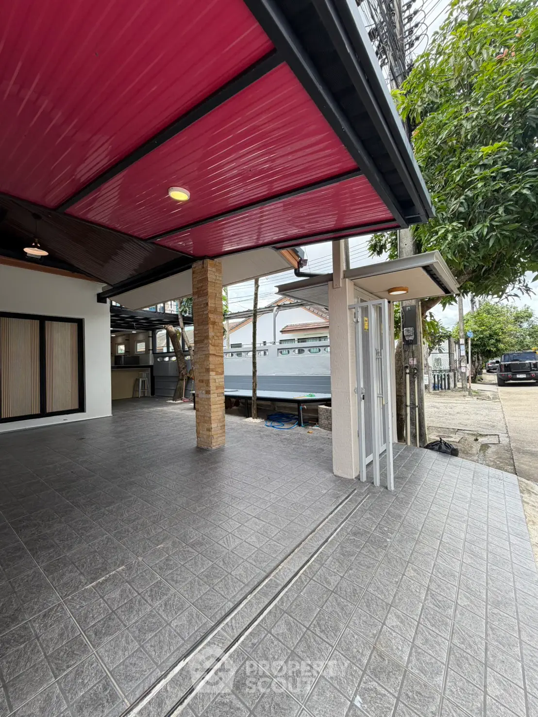 Modern residential entrance with covered parking and tiled flooring, featuring a vibrant red ceiling.