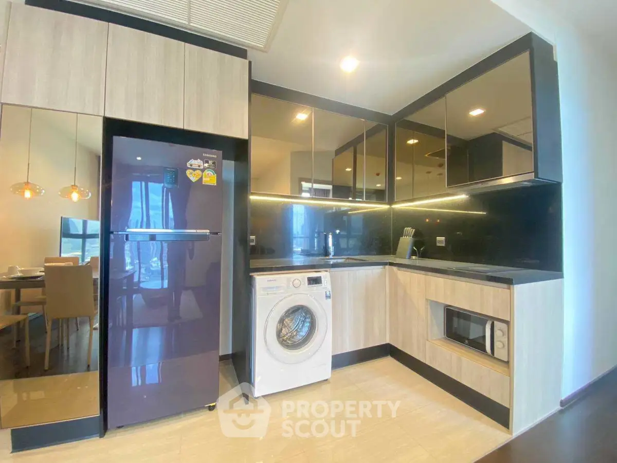Modern kitchen with sleek cabinets, washing machine, and dining area view.