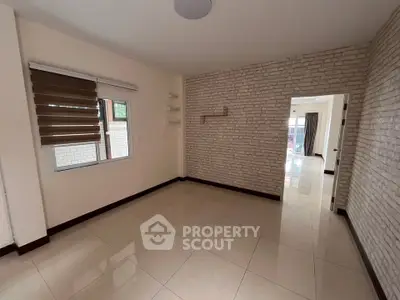 Spacious room with modern brick accent wall and large window, perfect for versatile living space.