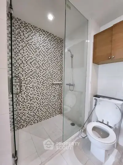 Modern bathroom with glass shower and mosaic tile wall in contemporary apartment.
