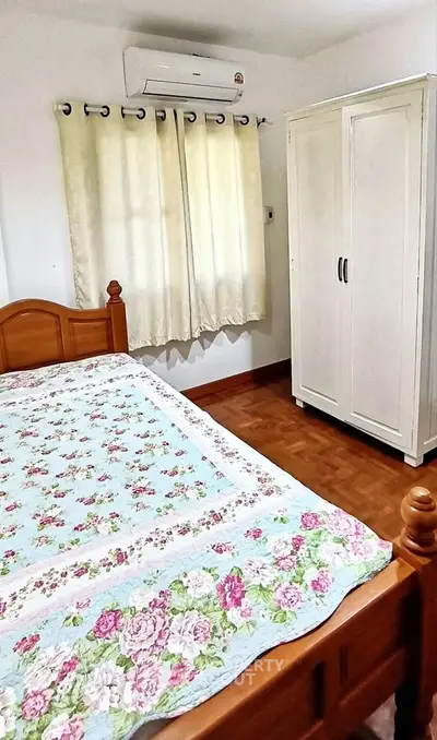 Cozy bedroom with floral bedding, wooden bed frame, and white wardrobe, perfect for a serene retreat.