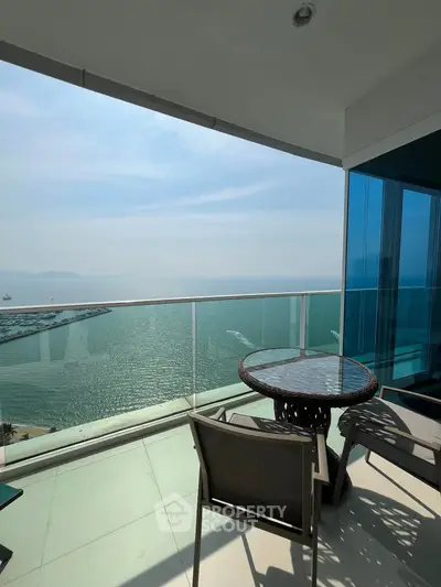 Stunning ocean view from a modern balcony with glass railing and outdoor seating.
