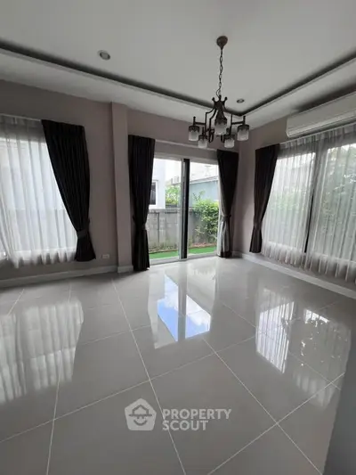 Spacious living room with large windows and elegant curtains, featuring glossy tiled floors and modern chandelier.