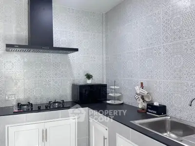 Modern kitchen with sleek black countertop, gas stove, and stylish patterned tiles.