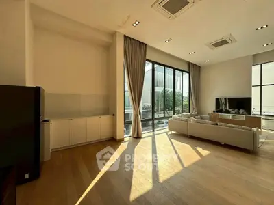 Spacious living room with large windows and modern decor, offering abundant natural light and a cozy ambiance.