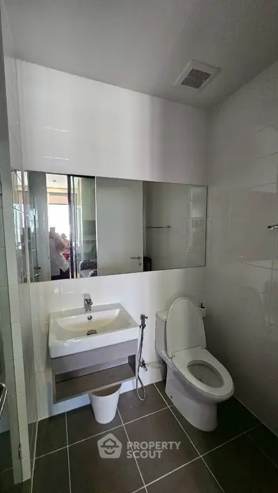 Modern bathroom with sleek fixtures and large mirror, featuring a toilet and sink.