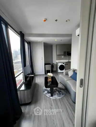 Modern living room with city view, featuring sleek furniture and integrated kitchen appliances.