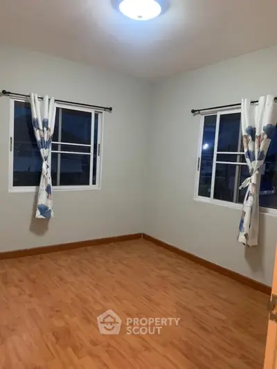 Spacious empty bedroom with wooden flooring and large windows.