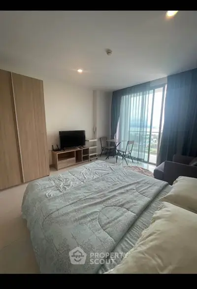 Spacious bedroom with balcony and modern furnishings in a high-rise apartment.