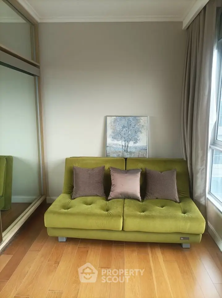 Stylish living room with green sofa and elegant decor, featuring large window and wooden flooring.