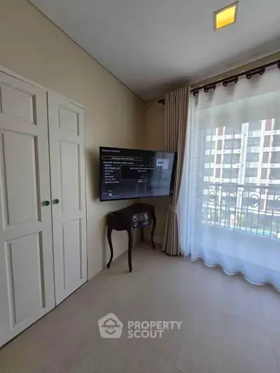 Bright living room with wall-mounted TV and large window offering city view.