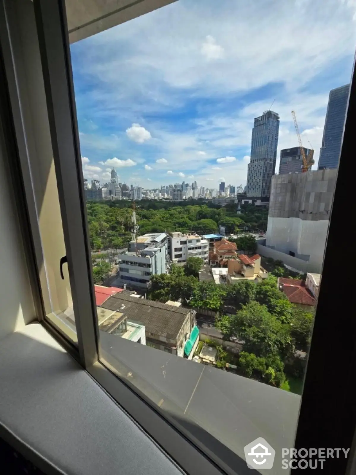 Stunning cityscape view from high-rise apartment window with lush greenery and skyline.