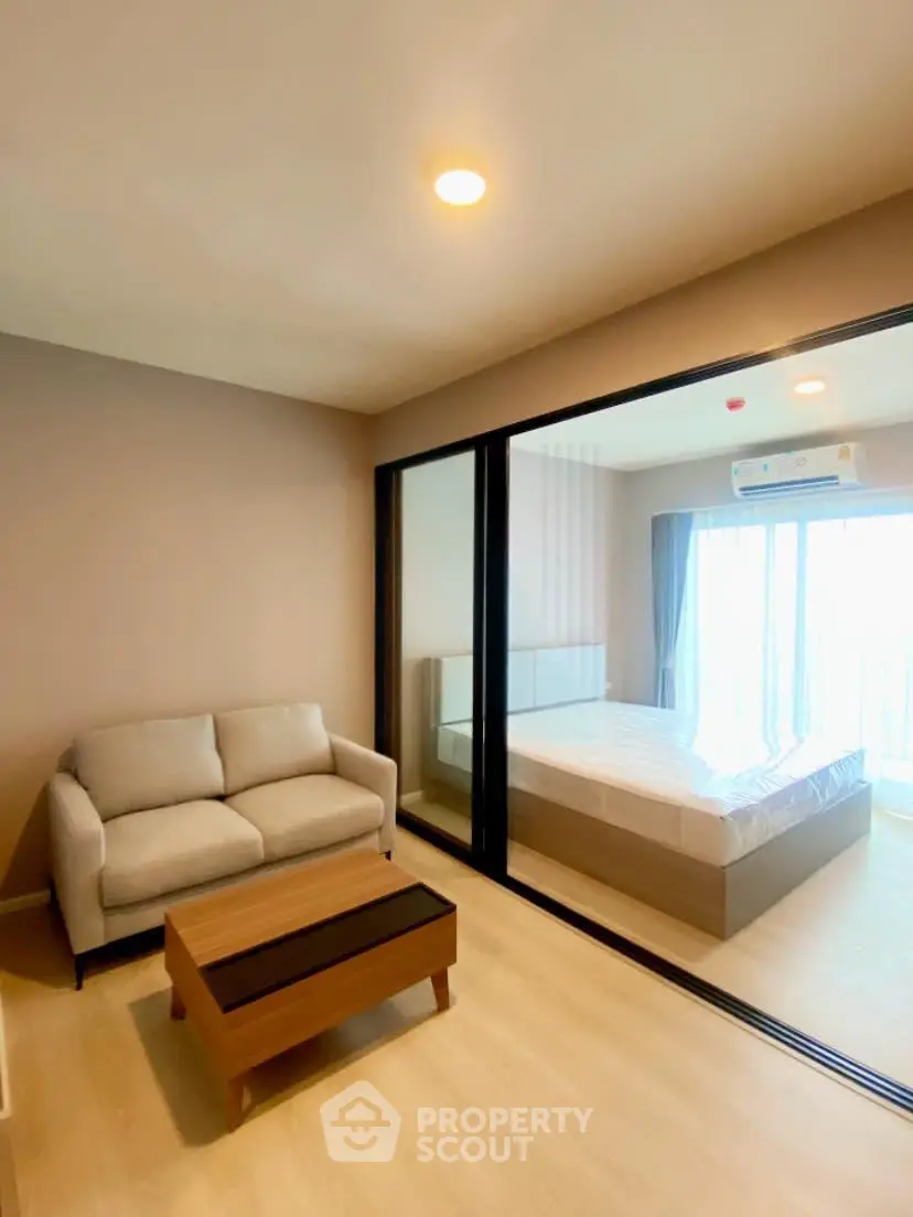Modern apartment interior with cozy living room and bedroom separated by glass partition.