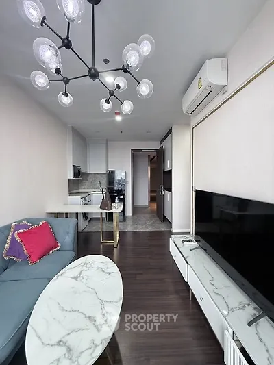 Modern living room with stylish chandelier, sleek furniture, and open kitchen layout in a contemporary apartment.