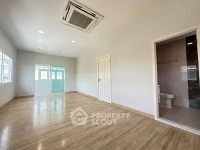 Spacious empty room with wooden flooring and modern ceiling air conditioning unit.